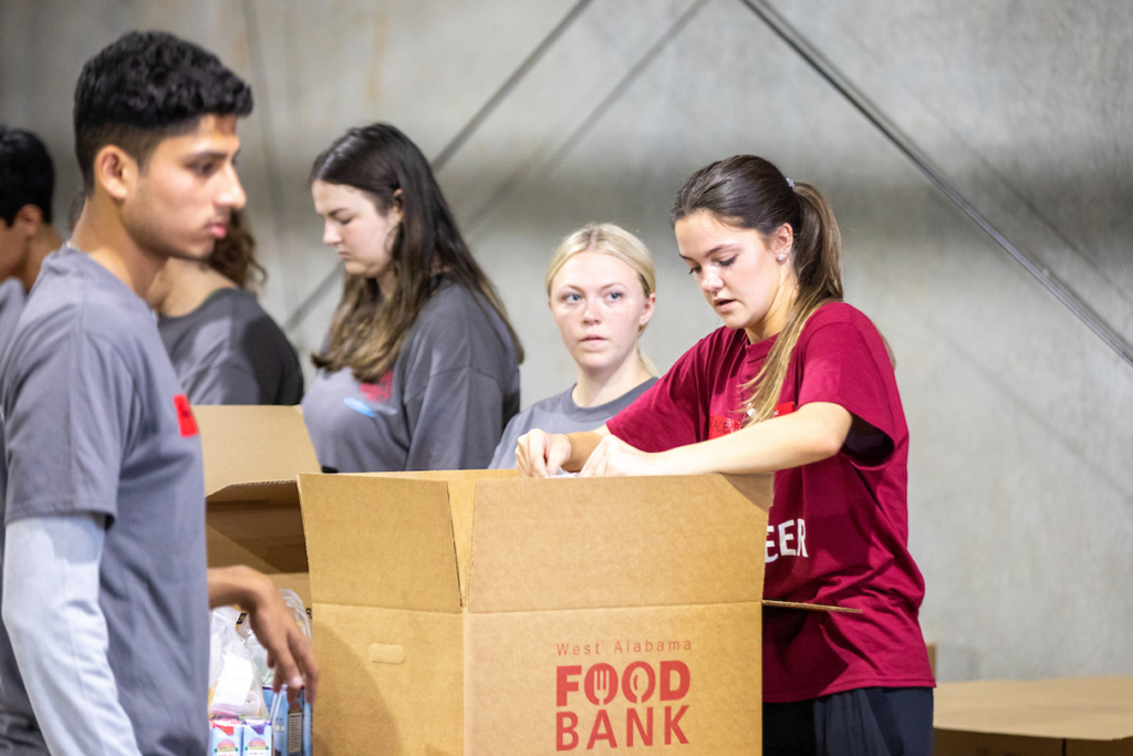 Student volunteers packing goods into a box at a food bank